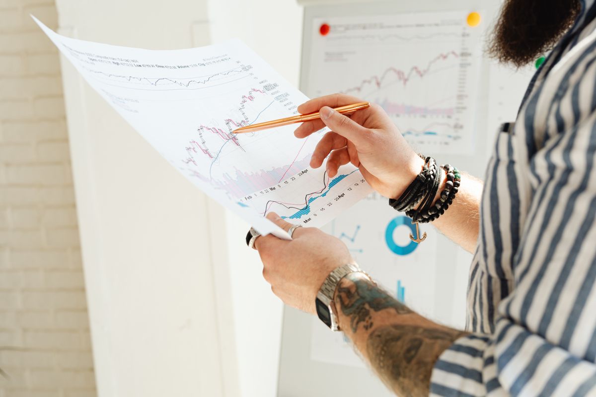 Axon Stock, Trump Trades, and ICE Contracts: A Market Story Driven by Timing, Trust, and Perception 3 A man analyzing stock market charts with a pen, holding a paper report indoors.