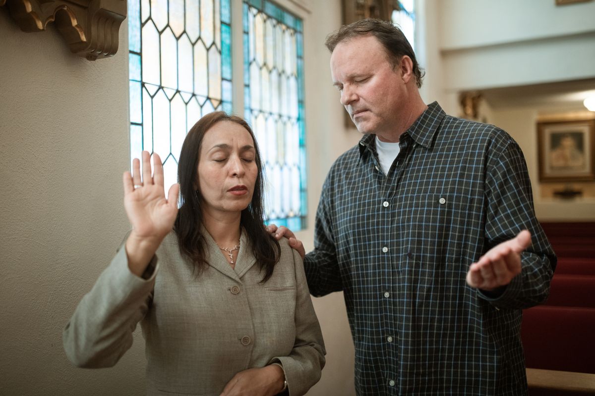 A man and woman praying together inside a church with stained glass windows.