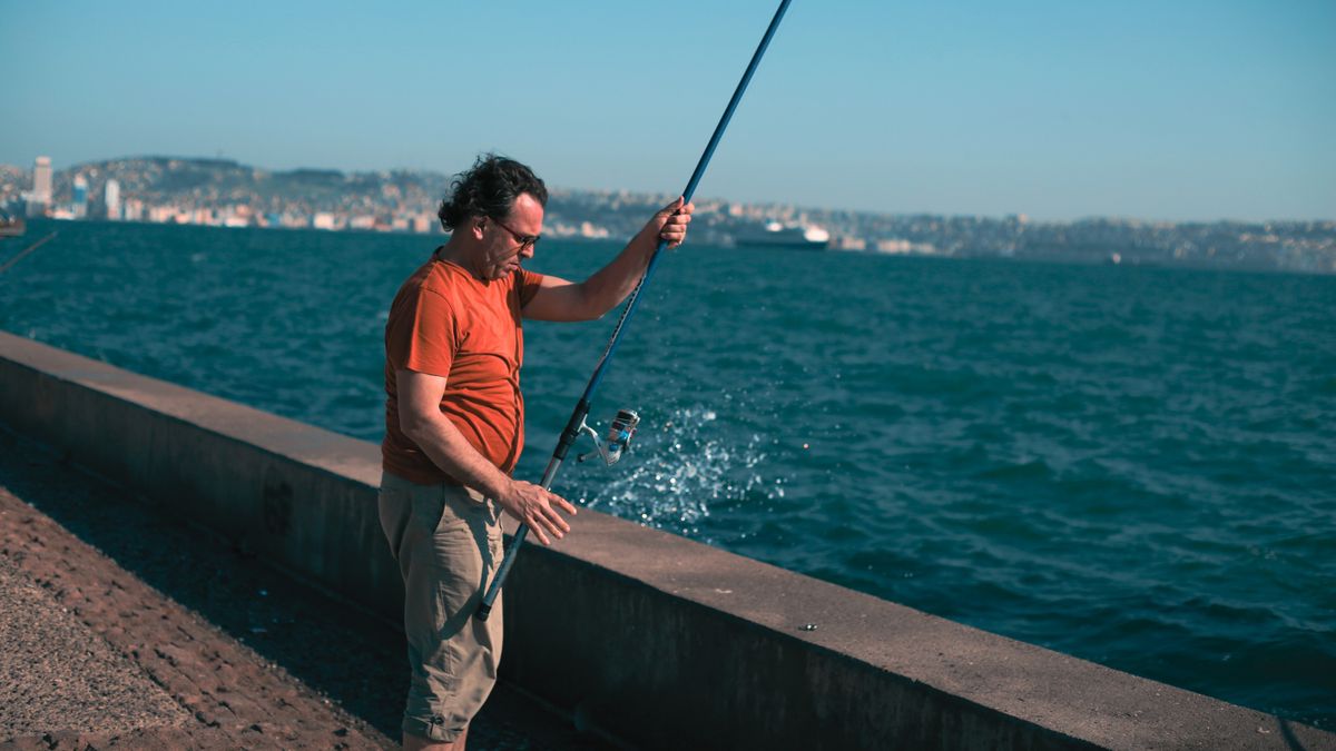 A man engaged in fishing along the İzmir waterfront with the cityscape visible in the background.