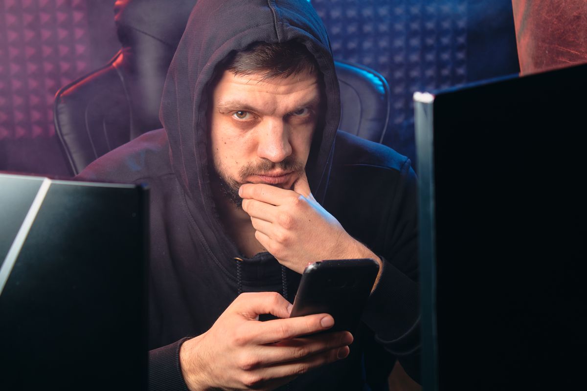 FBI Sounds Alarm as Scam Messages Surge Across Michigan While Residents Are Urged to “Take a Beat” Before Responding 1 A man in a black hoodie contemplating while using a smartphone, surrounded by digital screens.