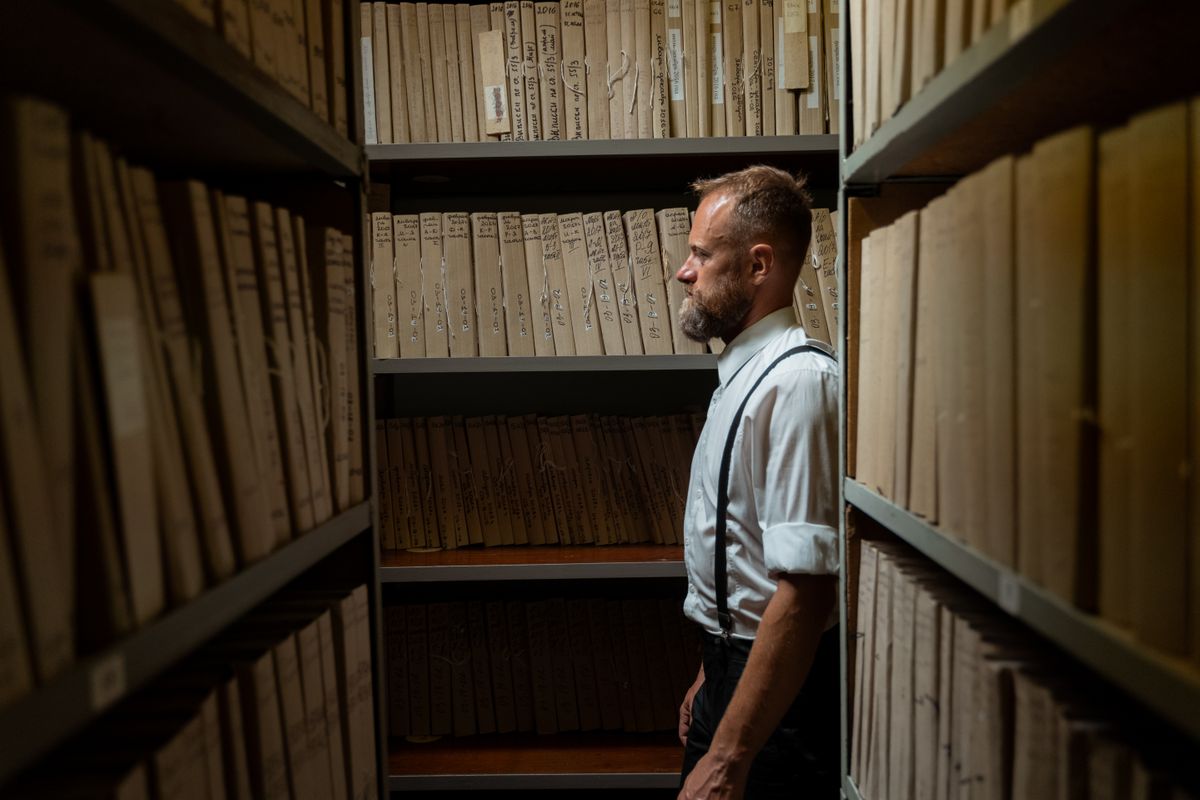 13 Costly Will Mistakes That Can Leave Families Fighting After You’re Gone 2 A man in formal attire and suspenders stands in an archive surrounded by documents.