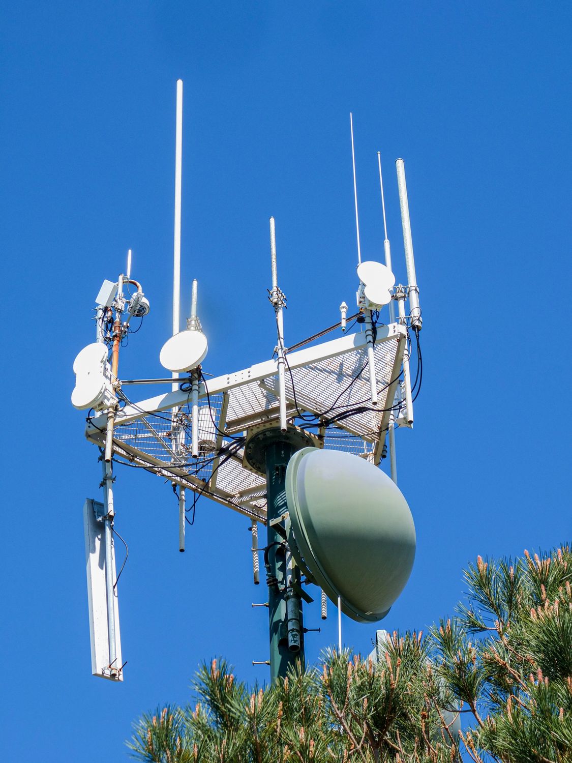 A modern antenna tower with various antennae and dishes, set against a vibrant clear blue sky.