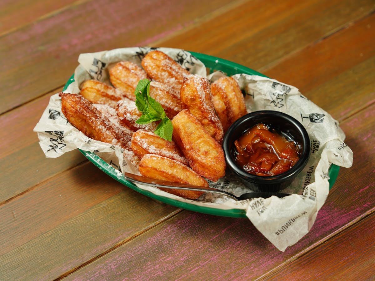 A mouth-watering platter of churros dusted with sugar alongside a tangy dipping sauce, perfect for dessert cravings.