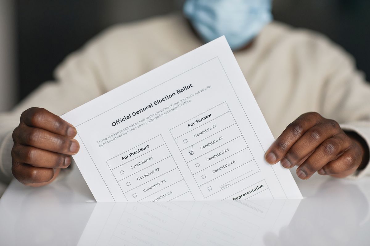 A person wearing a face mask holds an official general election ballot.