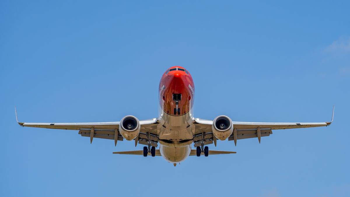 A red commercial airplane captured landing against a clear blue sky at Manises Airport, Spain.