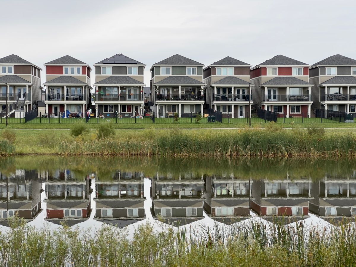 A row of modern houses reflected in a calm pond, showcasing serene suburban architecture.