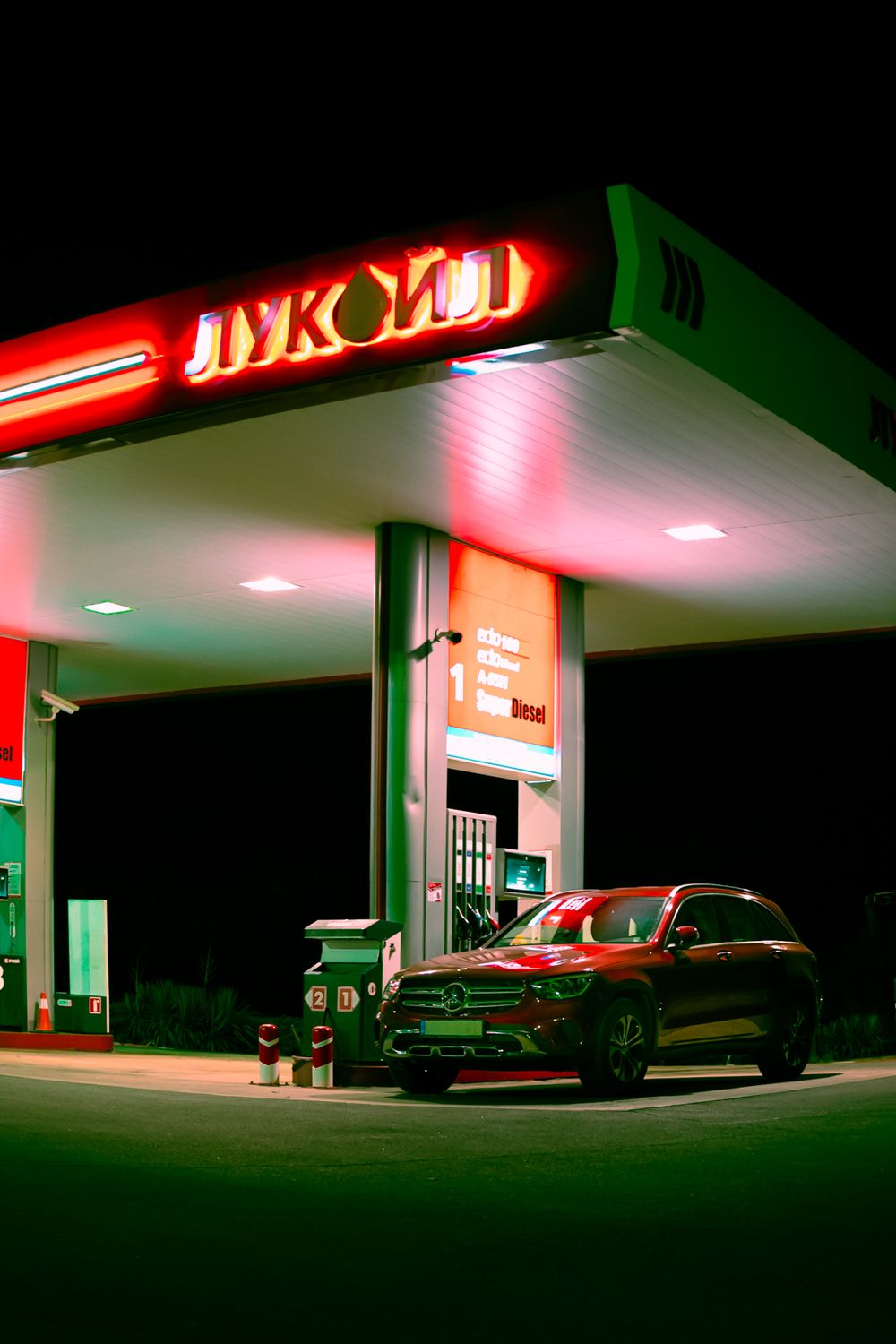 A sleek car parked at a brightly lit gas station under a neon sign during nighttime.