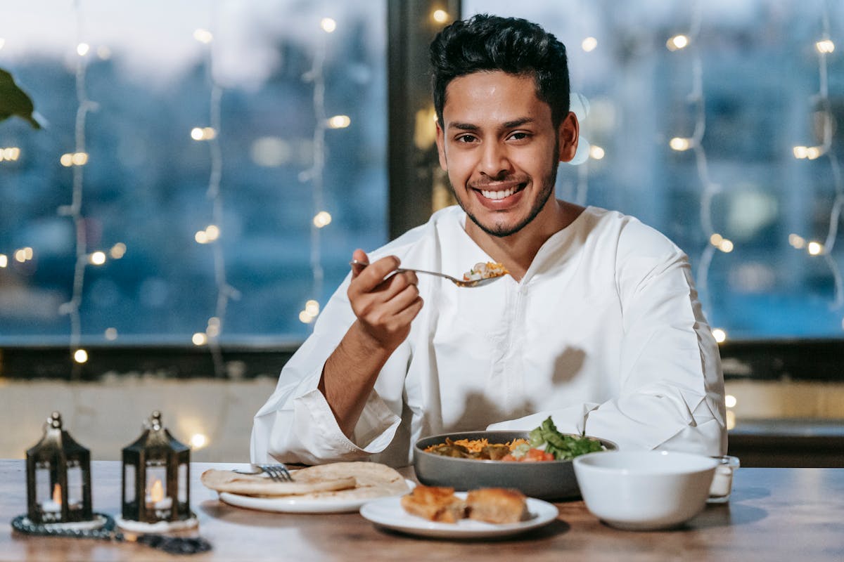 A smiling man enjoys a traditional meal indoors, surrounded by string lights.