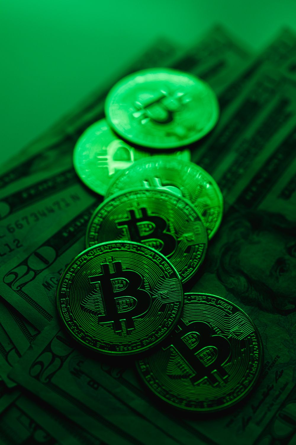 Six shocking fraud cases from 2024 show how fast money, trust, and technology can be turned against ordinary people. 2 A stack of Bitcoin coins atop US dollar bills illuminated by green lighting, symbolizing digital finance and cryptocurrency.