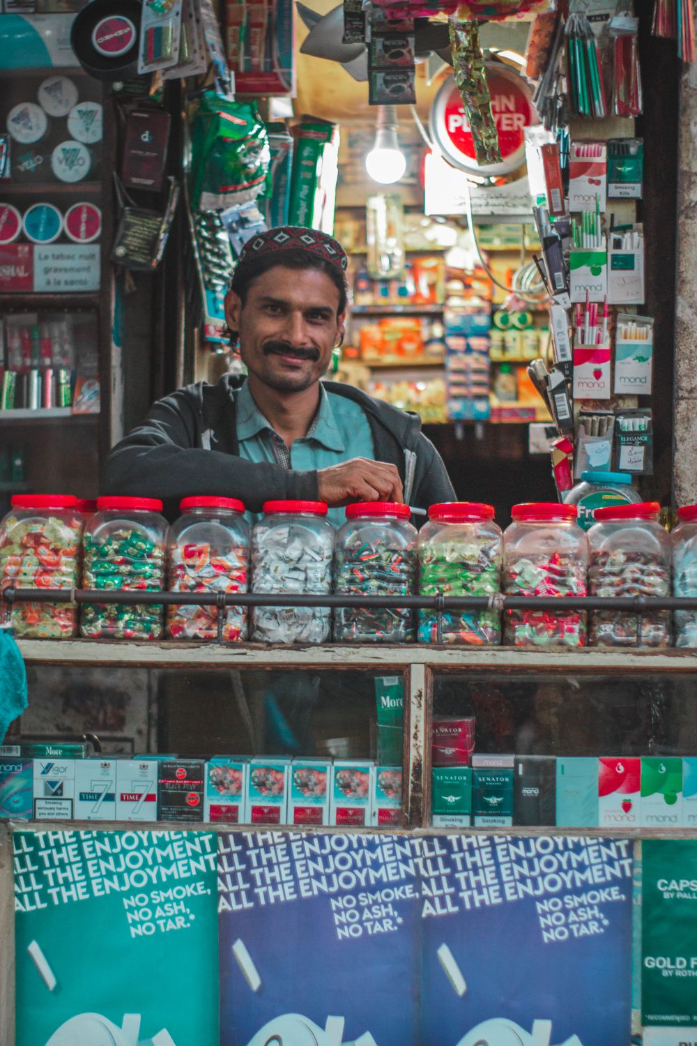 A street vendor with candy jars and products in a vibrant urban market setting.