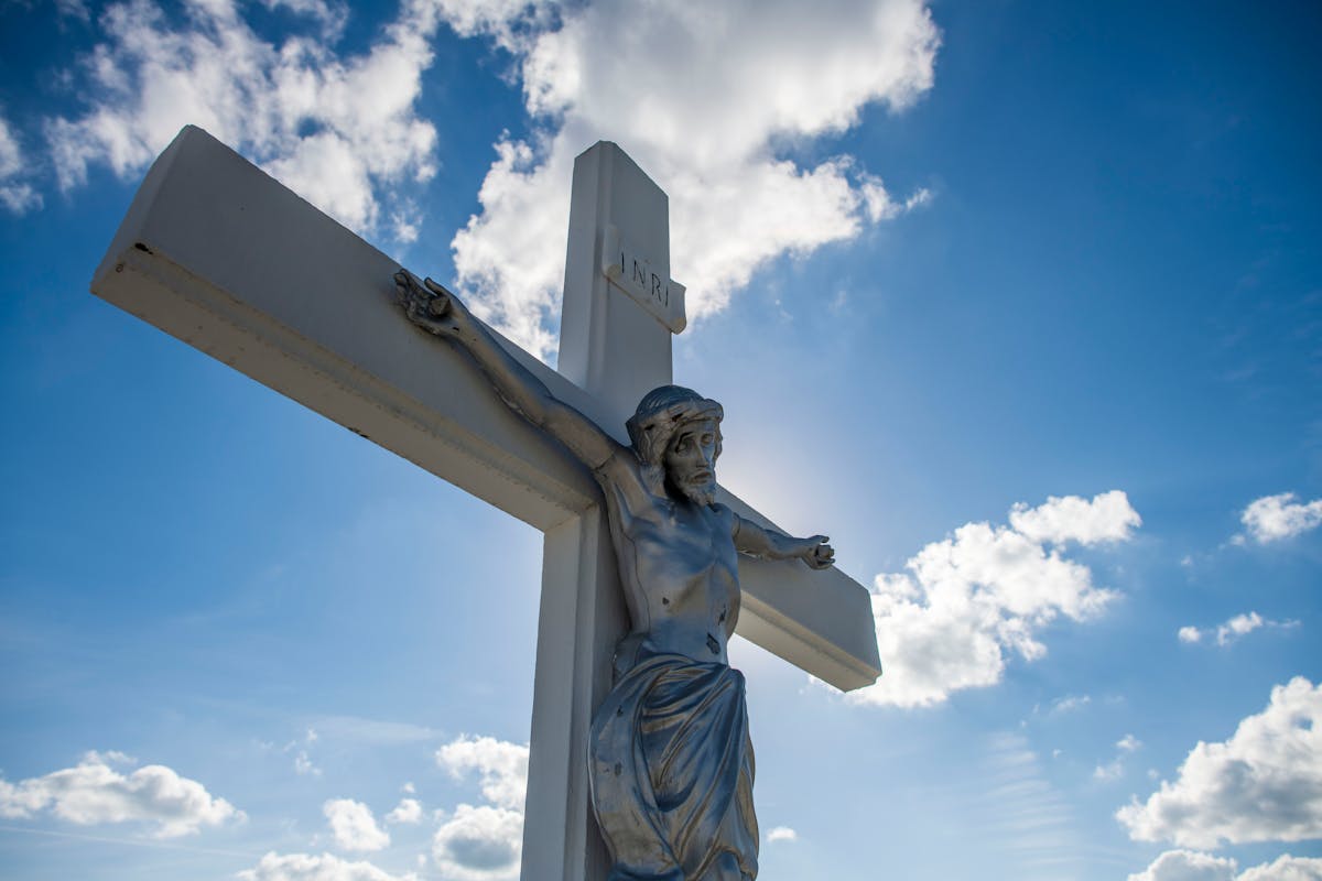 10 Reasons Jesus Kept the Scars That Death Couldn’t Erase 2 A striking sculpture of Jesus on the cross with a vivid blue sky background.