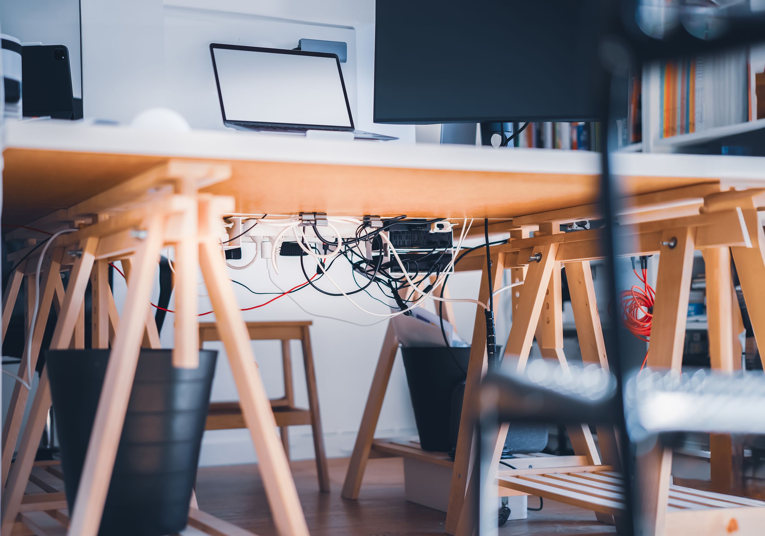 A stylish workspace with visible cables, laptop and monitor, highlighting modern technology's complexity.