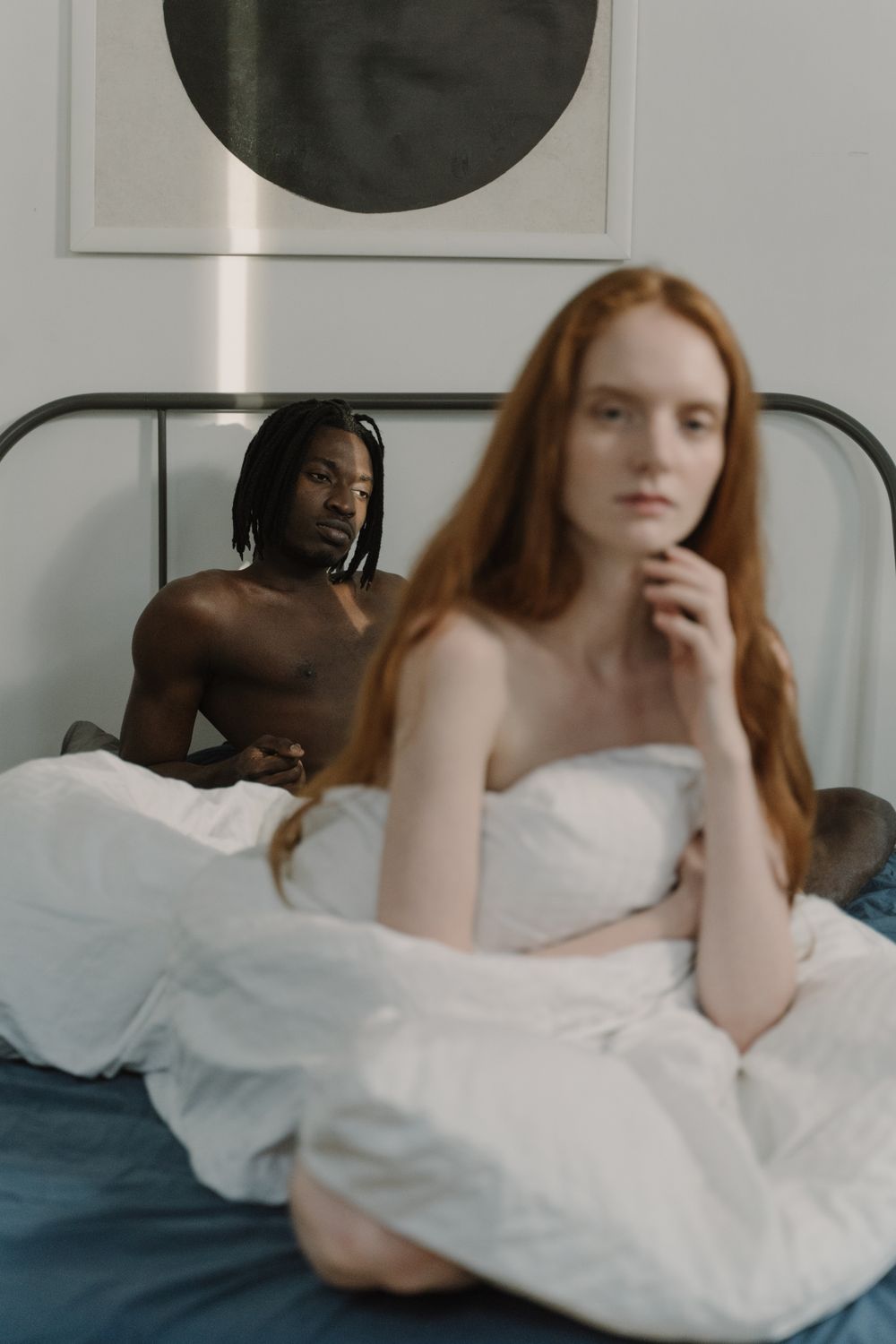 A thoughtful couple sitting together in a minimalist bedroom, evoking connection and intimacy.
