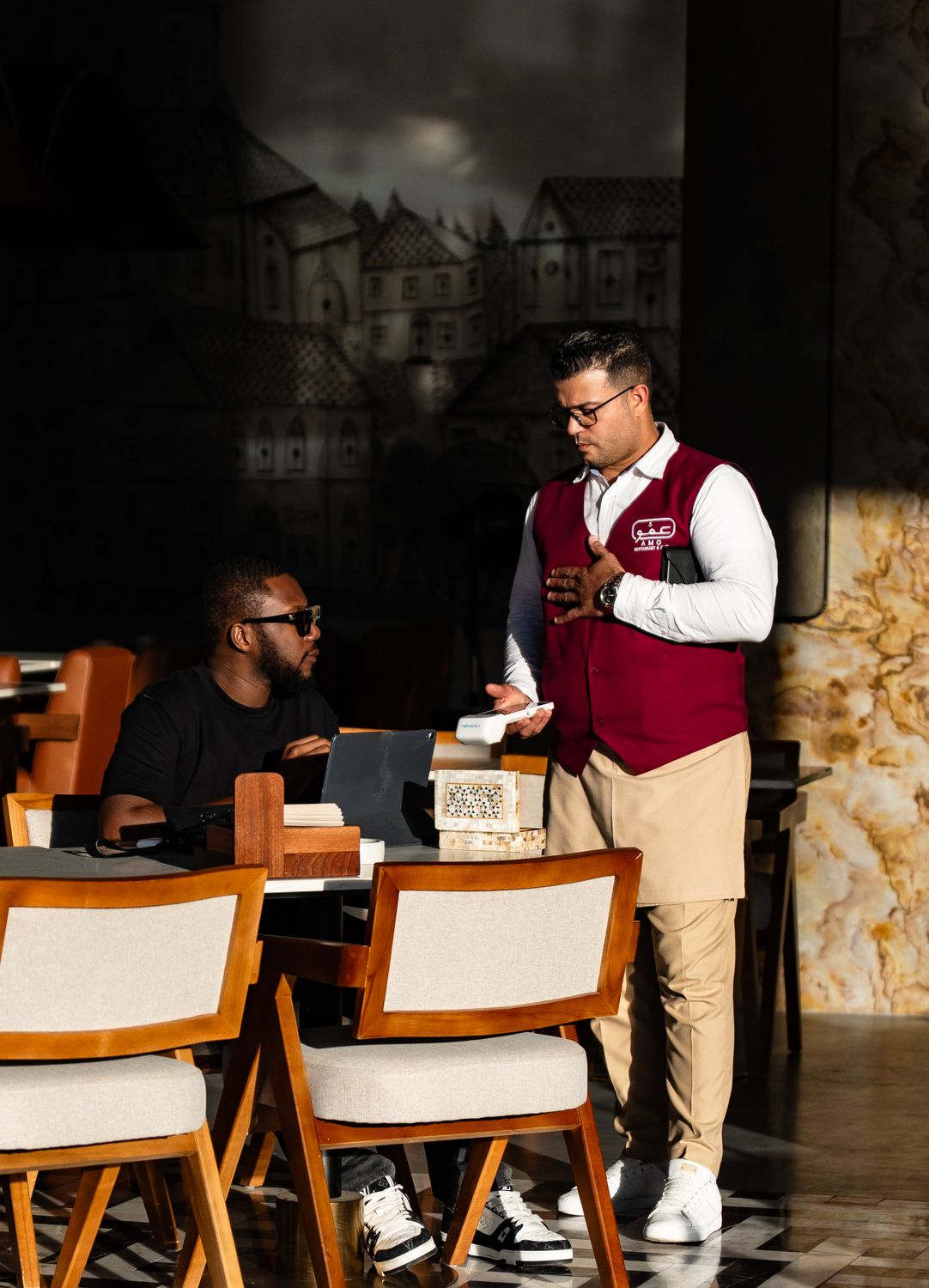 From Kitchen Idea to Thriving Brand: The Real Playbook for Starting a Food Business 4 A waiter in uniform serves a customer in a trendy Dubai cafe with unique decor.