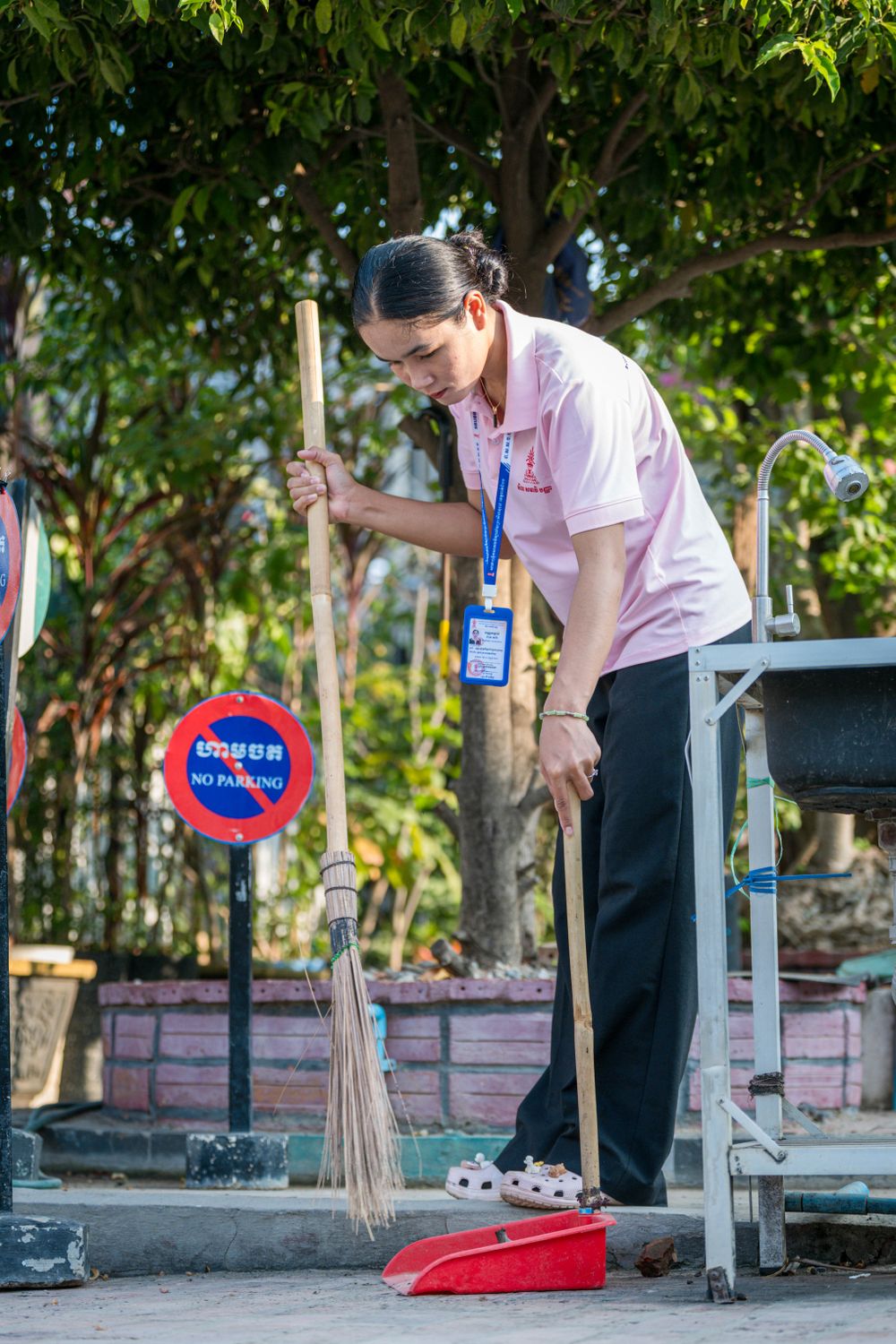 8 Hard Truths Washington Families Should Know Before Wild Waves Closes for Good 3 A woman cleaning a park area in Krong Battambang, Cambodia, using a broom and dustpan.