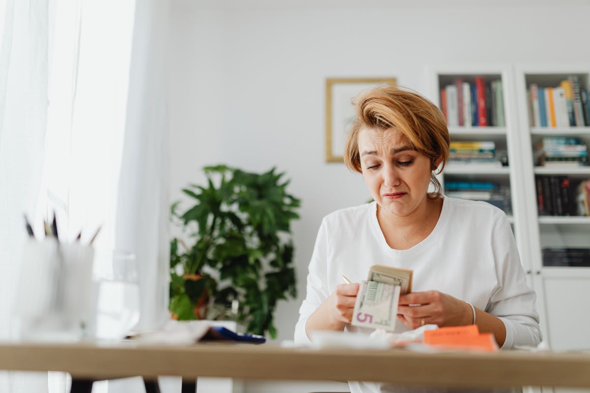 10 Things Americans Should Know When a Country Runs Out of Money 3 A woman concernedly counts money at her desk in a bright room.