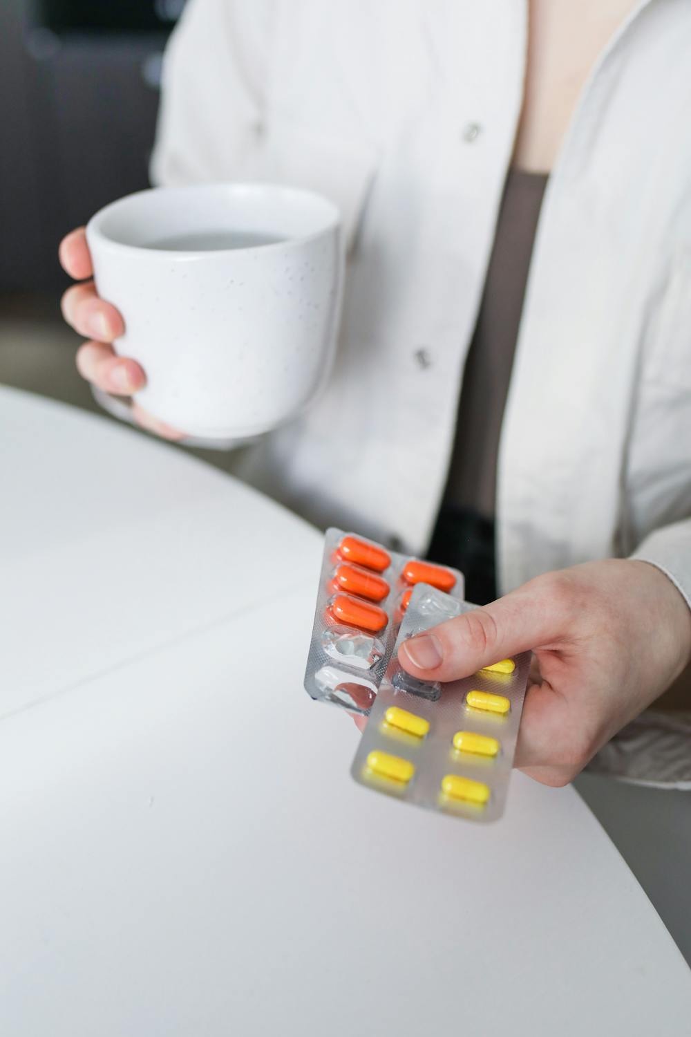 9 Daily Coffee Mistakes That Are Quietly Harming Your Health 2 A woman holding blister packs of pills and a mug of tea, symbolizing treatment for illness.