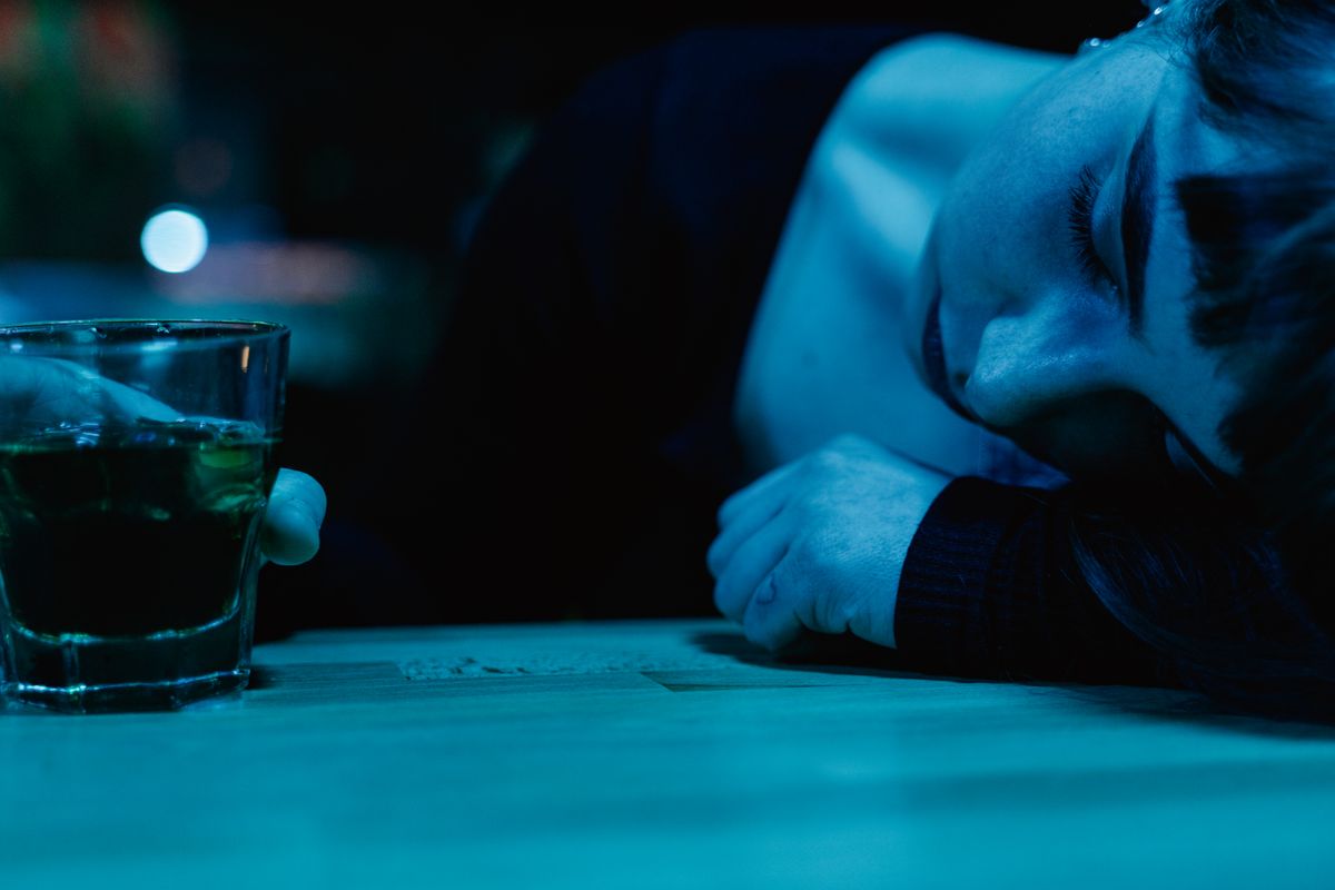 A woman rests on a table next to a glass of drink, illuminated in blue light.