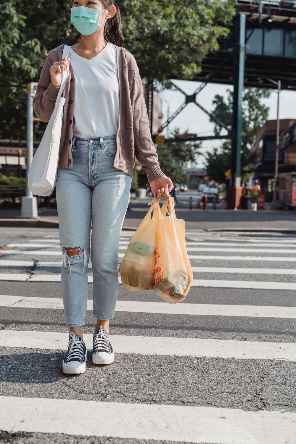 A woman uses a crosswalk while carrying shopping bags and wearing a face mask.