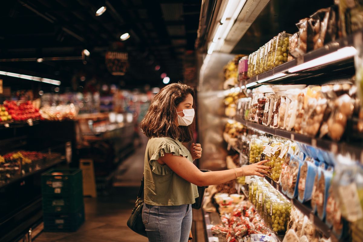 A woman wearing a mask shops for groceries in a supermarket aisle.