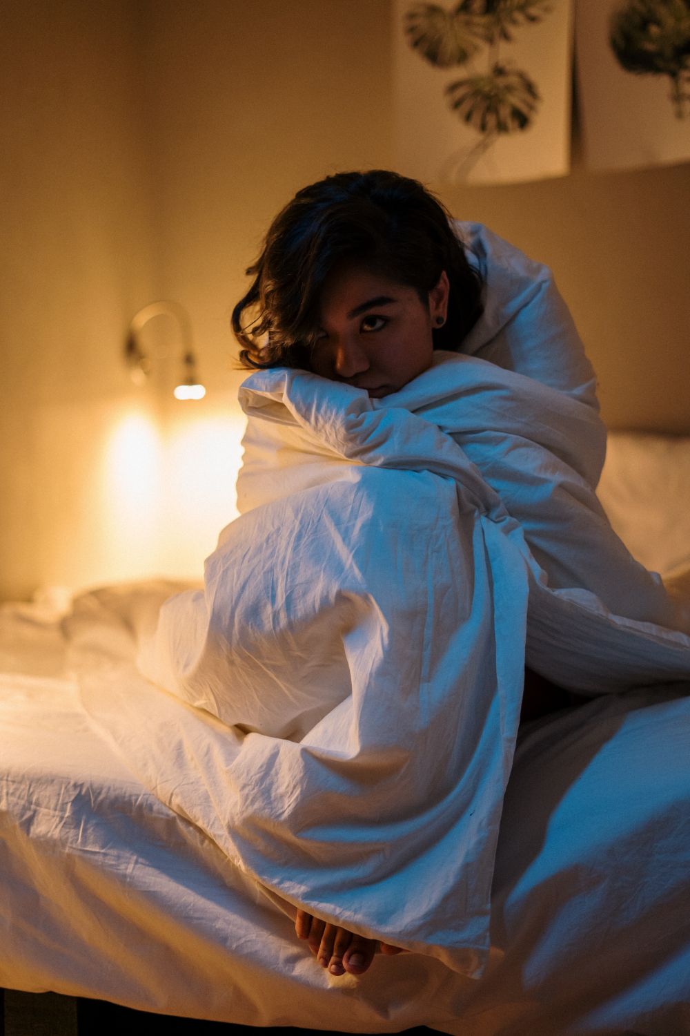 A woman wrapped in a blanket, creating a cozy vibe in her warmly lit bedroom.