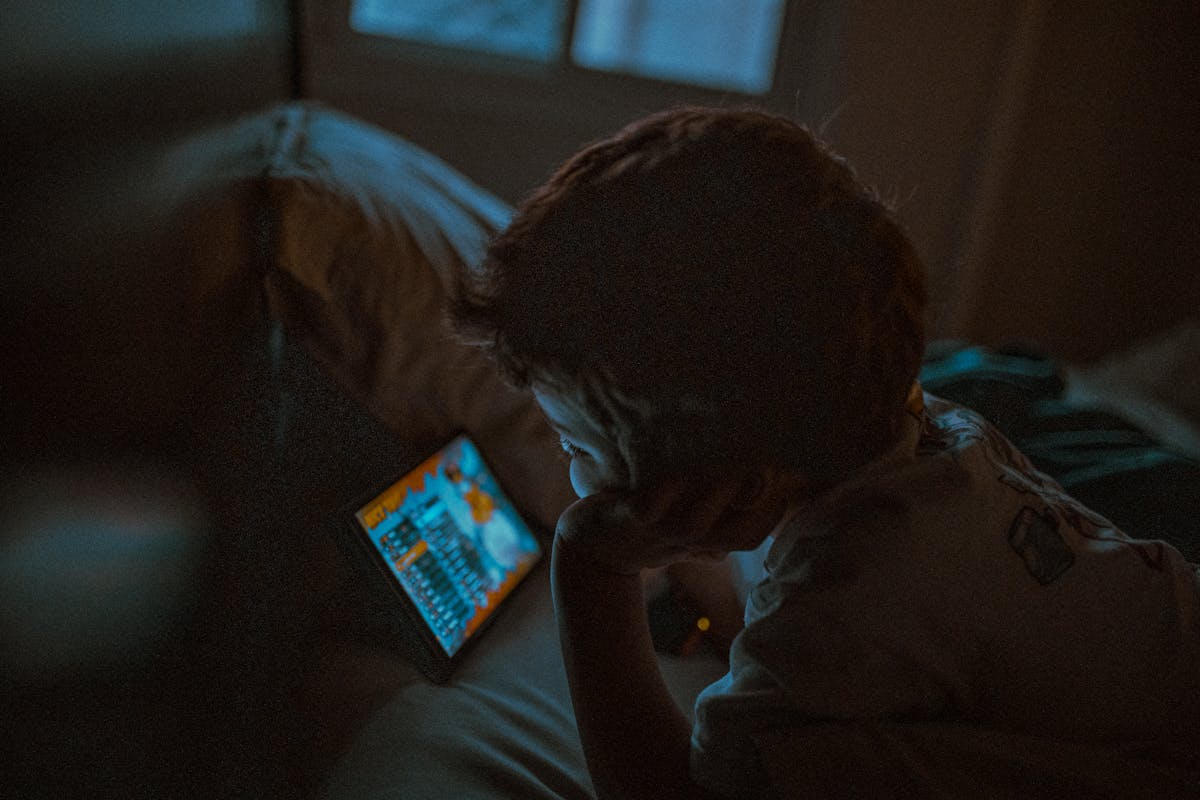 You’re Slowly Ruining Your Life by Ignoring These 9 Lifestyle Habits 3 A young child is intently watching a tablet in a cozy, dimly lit room, creating a serene nighttime ambiance.
