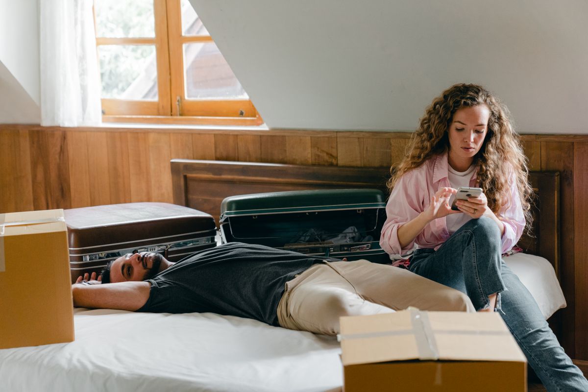Florida’s Renter Crisis Hits Catastrophic Levels: Millions Facing Eviction and Financial Ruin in 2026 2 Adult ethnic man lying on bed while woman with curly hair using smartphone sitting near and relaxing among suitcases and cardboard boxes for moving
