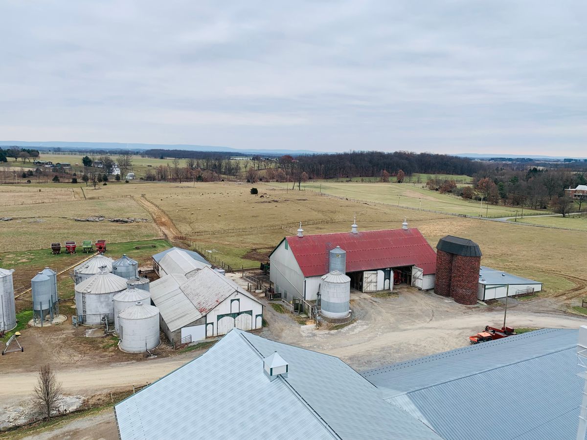 Aerial view of a Maryland farm with barns and silos under a cloudy sky.