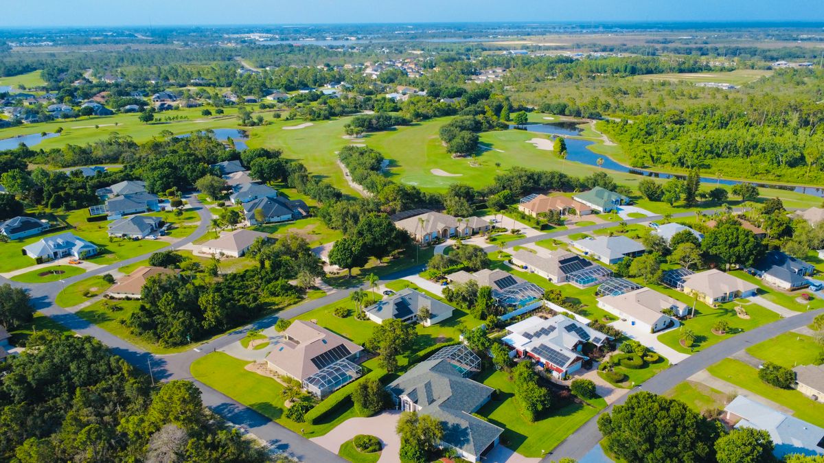 Aerial view of a sunny suburban neighborhood with green landscapes and solar-powered homes.