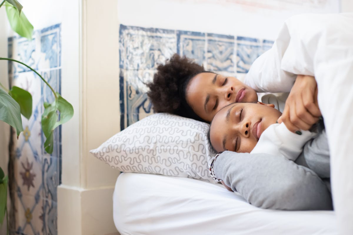 African American mother and daughter sleeping together in bed, showing love and warmth.