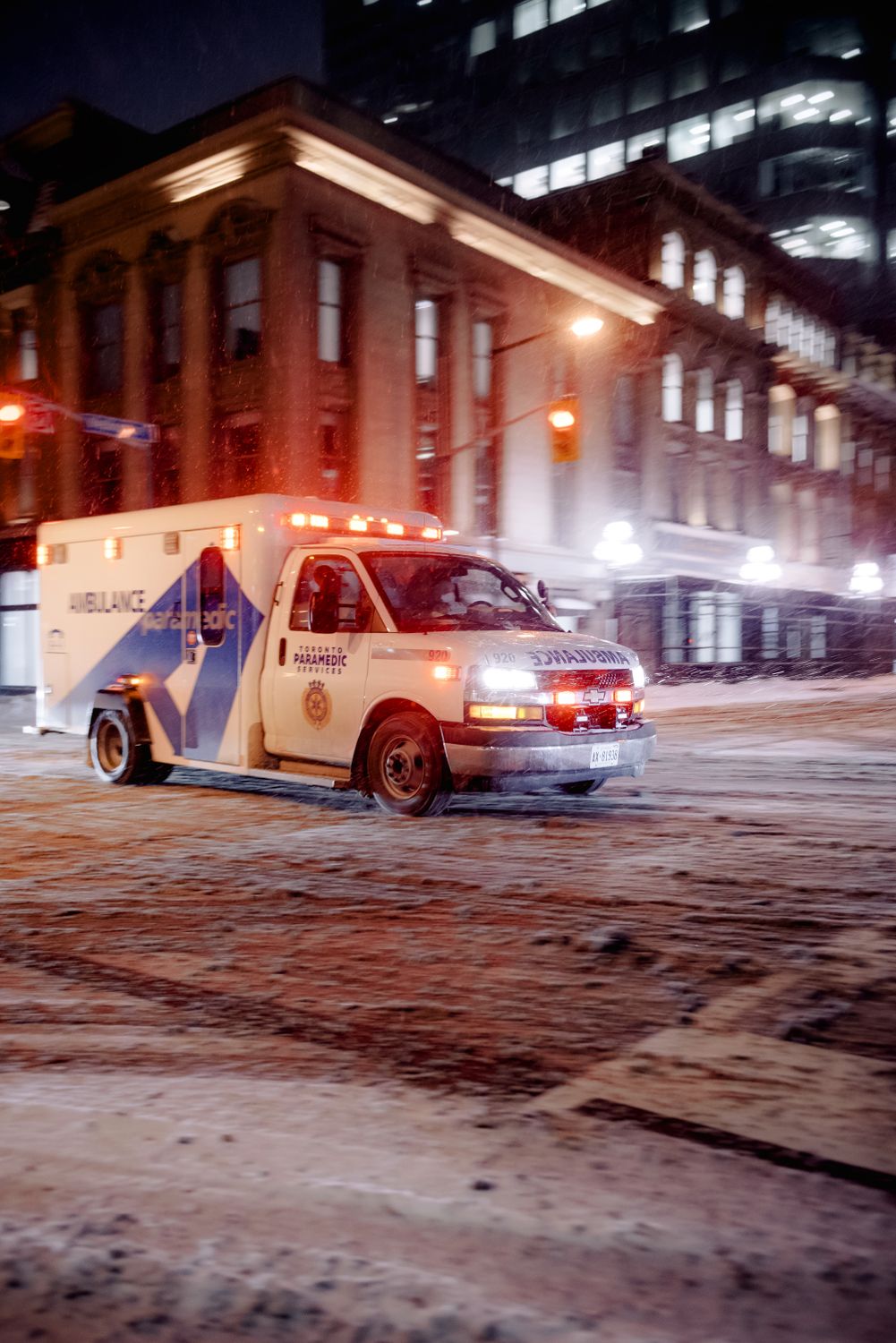 Ambulance driving through snowy city streets at night, highlighting emergency response in winter conditions.