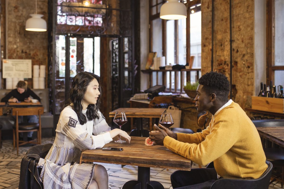 8 First-Date Questions Women Secretly Wish More Men Would Ask in 2026 2 An Asian woman and Black man enjoy a romantic date with wine in a stylish café.
