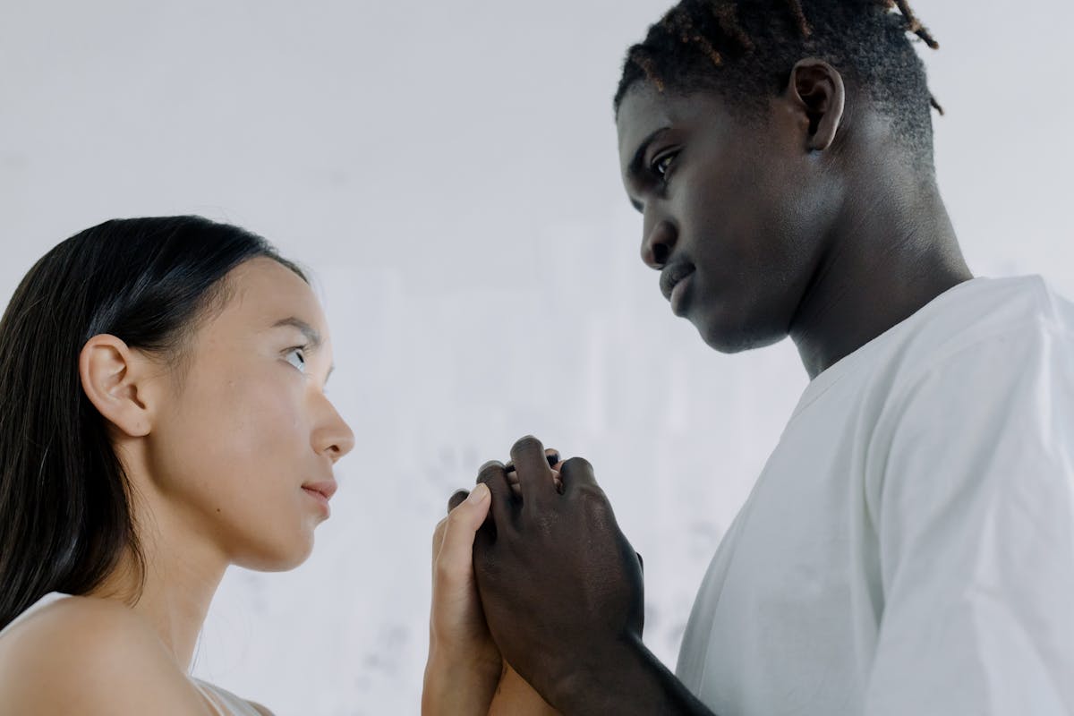 7 Painful Signs You’re More Like A Responsibility Than A Partner To Him 3 An interracial couple, a black man and an Asian woman, engage in a tender moment indoors, holding hands and looking into each other's eyes.