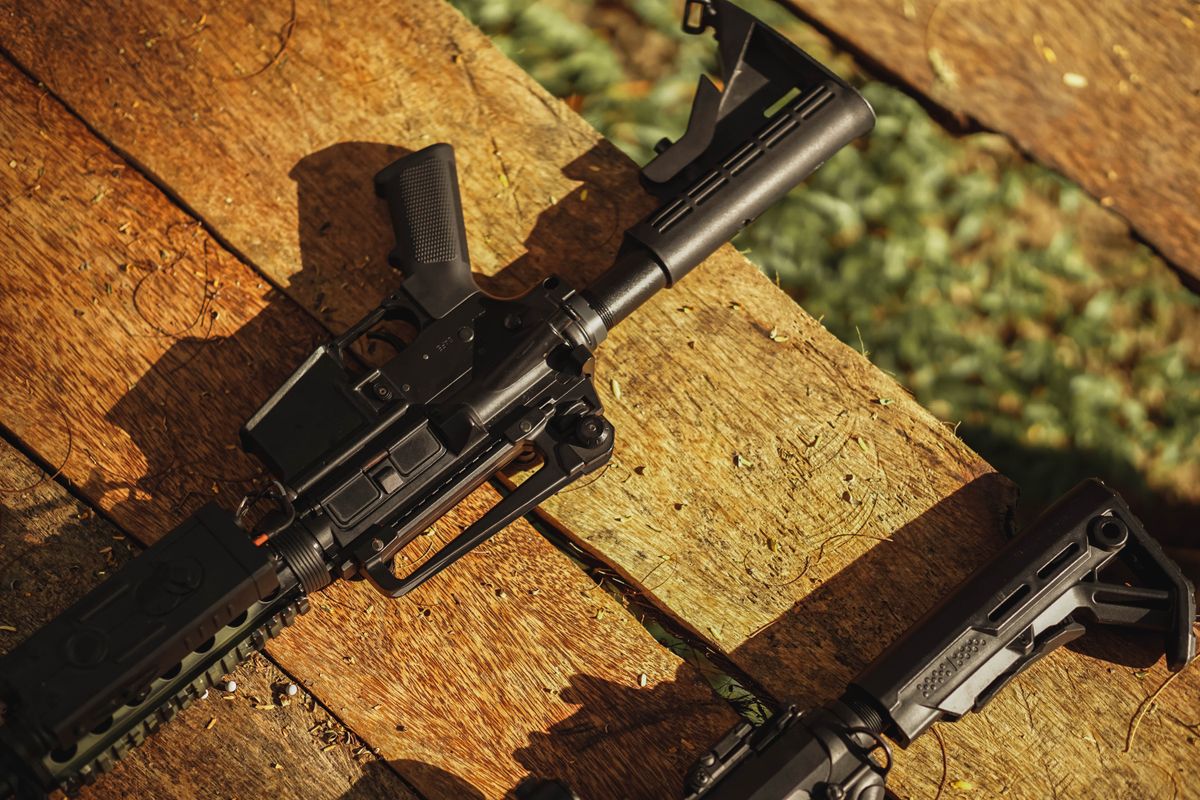 AR-style rifle displayed on wooden planks in natural light, showcasing tactical features.