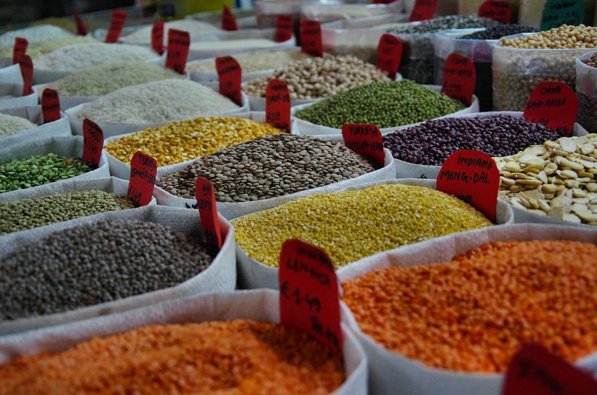 Grocery Prices Are Out Of Control: 10 Items to Grab Before Costs Soar Again 4 Bags of vibrant grains and spices on display in a bustling market setting.