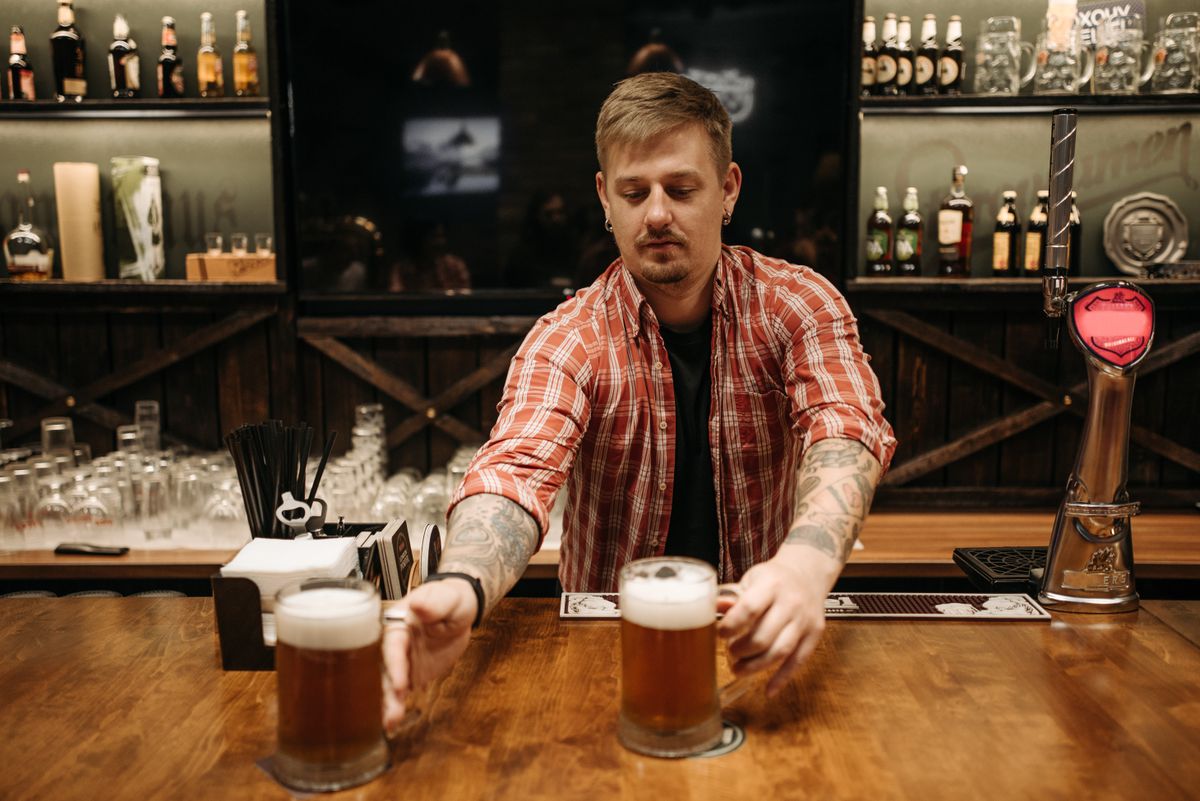 Bartender serving two pints of beer at a cozy bar counter.