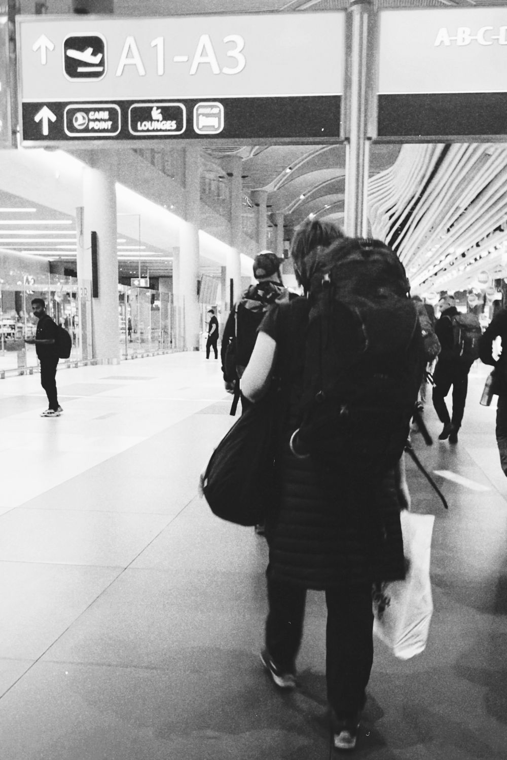 Black and white scene of travelers walking through İstanbul Airport terminal.