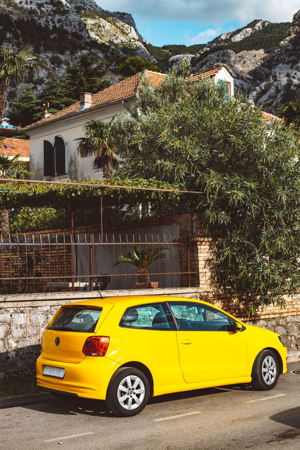 Bright yellow car parked on a picturesque street with mountainous backdrop.