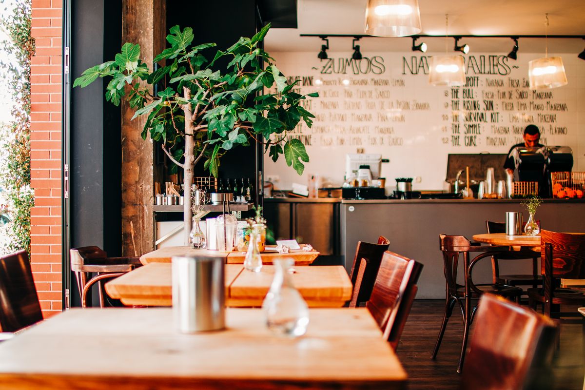 Austin Restaurant to Close After 10 Years as Rising Rent, Construction, and Empty Tables Push It to the Brink 1 Charming cafĆ© interior in AndalucĆa, Spain featuring wooden tables and lush plants.