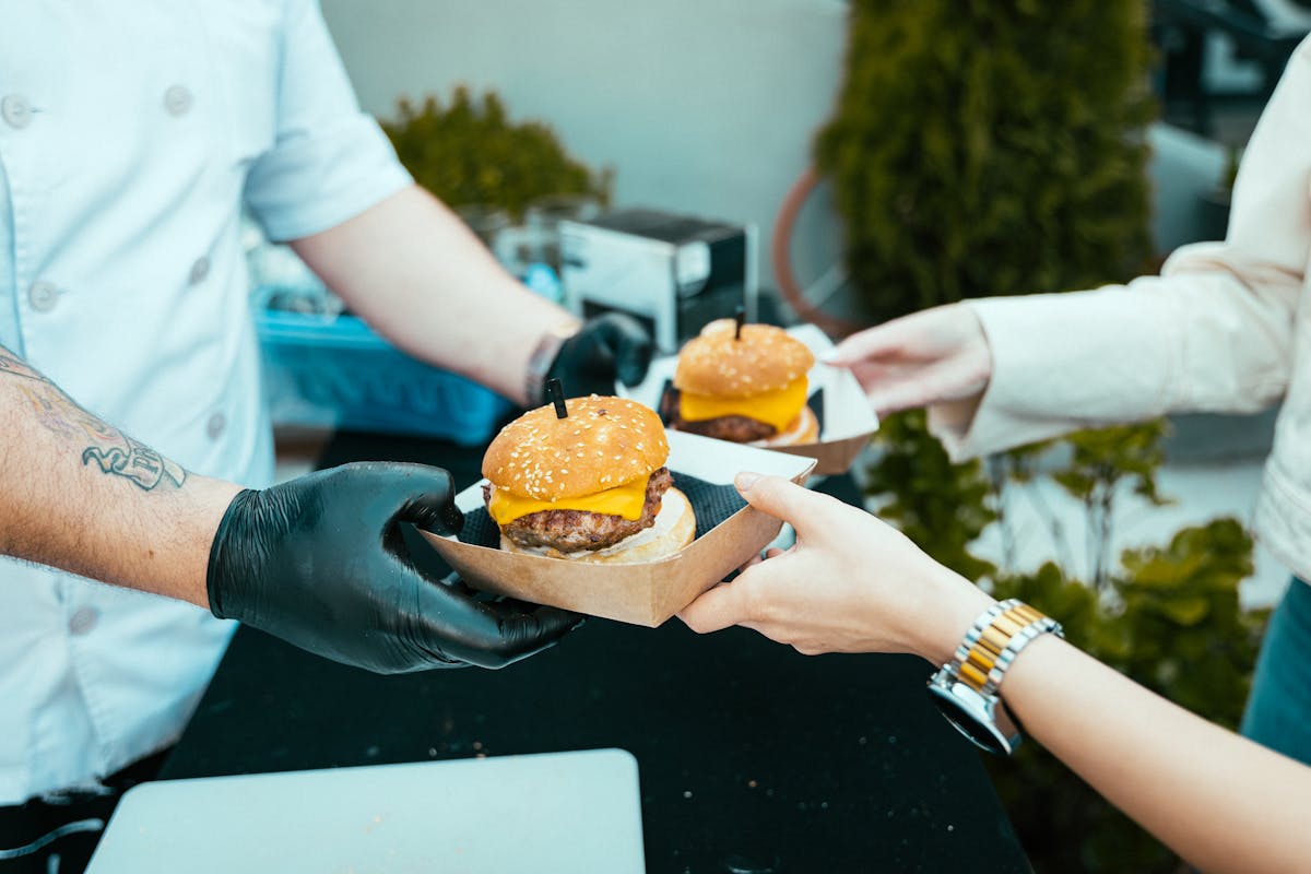 Wendy’s Branding Catastrophe: How the New Blue Makeover Risks Killing Appetite and Loyalty 2 Chef hands over delicious cheeseburgers to a customer at an outdoor food stall.