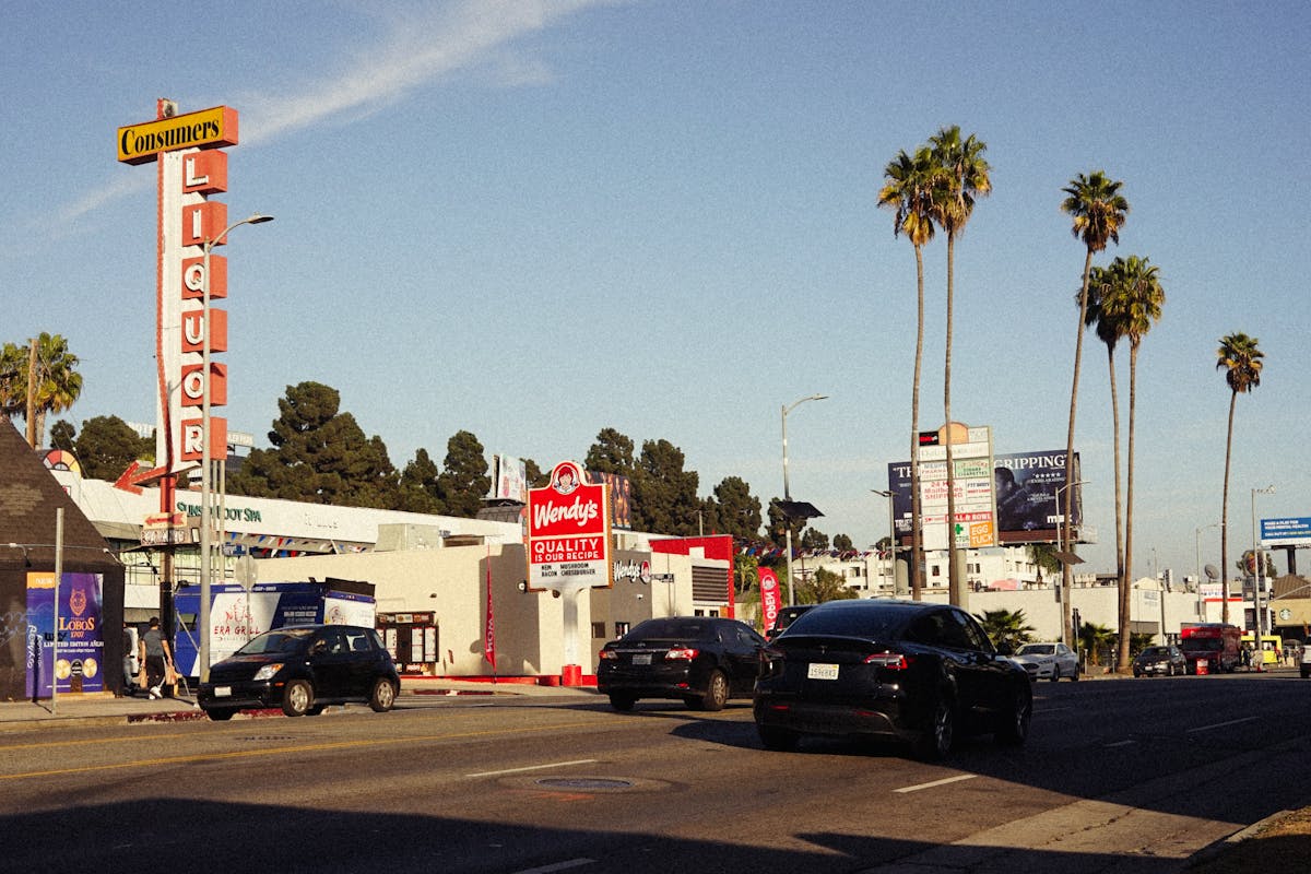 Wendy’s Branding Catastrophe: How the New Blue Makeover Risks Killing Appetite and Loyalty 4 City street with cars, palm trees, and various signs under a clear sky.