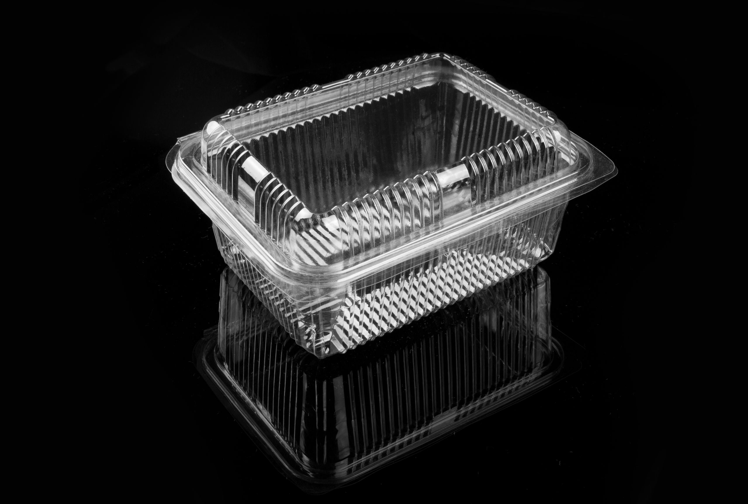 Clear plastic food container on a black reflective surface, minimalist style.