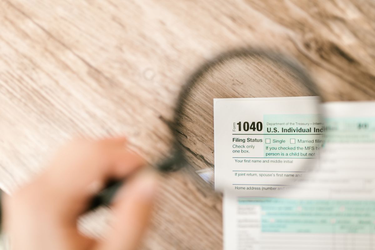 Trump IRS Audit Immunity Under Scrutiny as Former Officials Challenge Settlement Deal 1 Close-up image of IRS Form 1040 under a magnifying glass on a wooden surface.