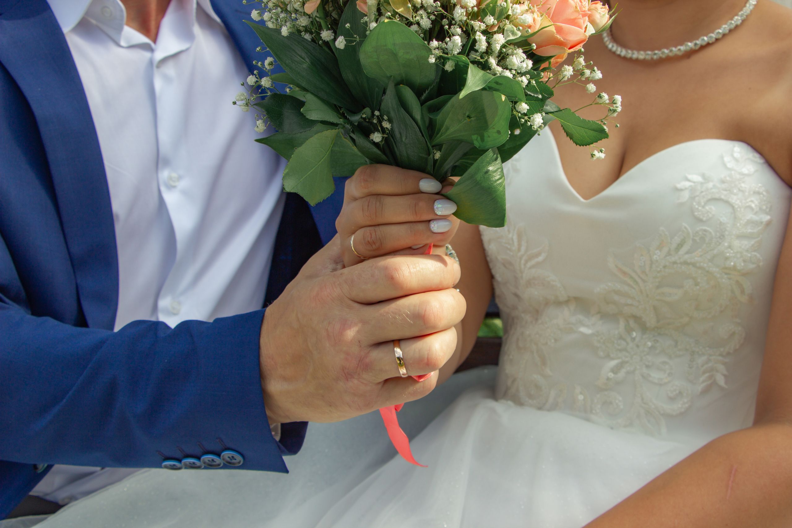 Close-up of a bride and groom holding a floral bouquet, symbolizing love and commitment.