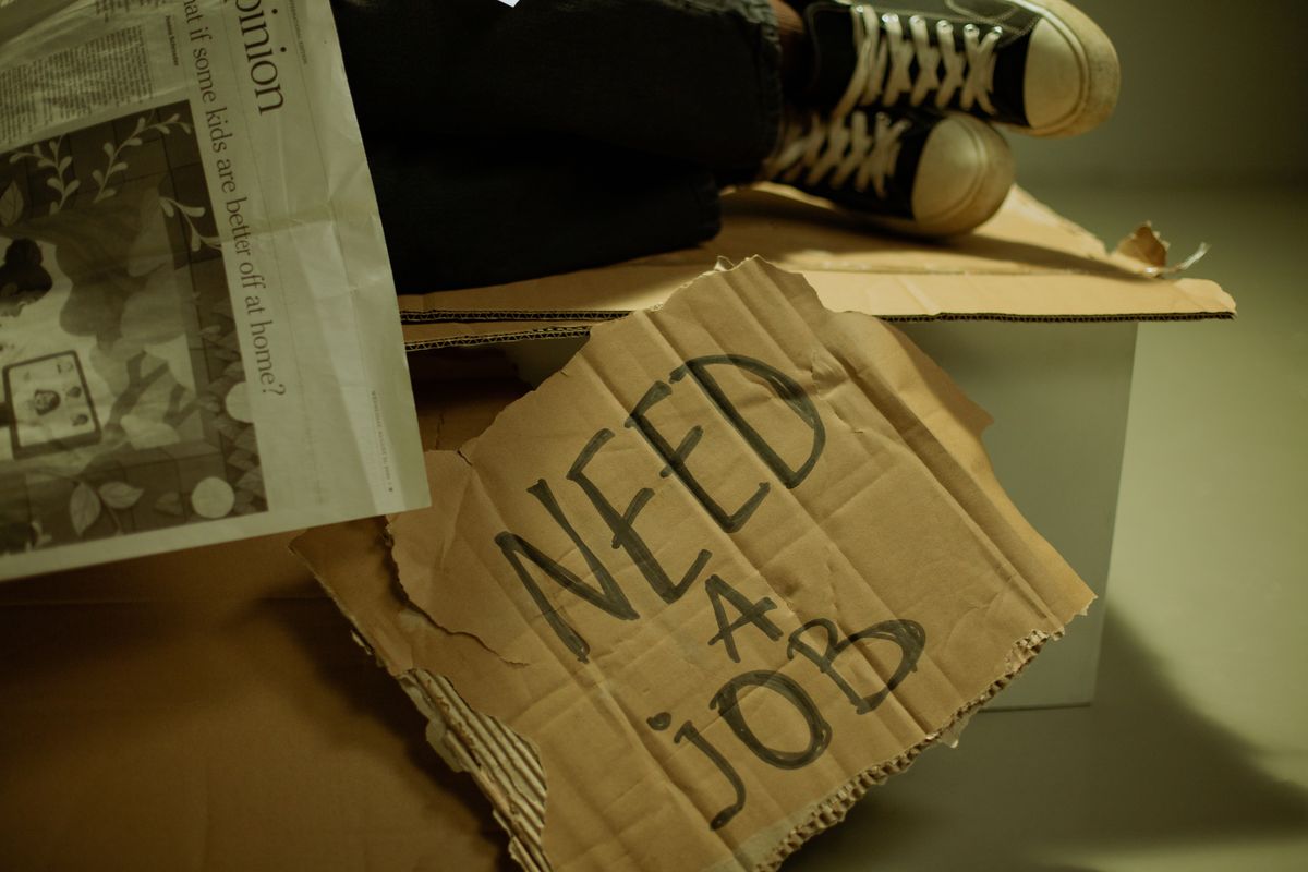 Close-up of a cardboard sign and newspaper depicting joblessness and unemployment.
