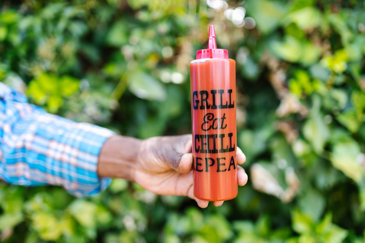 Close-up of a hand holding a ketchup squeeze bottle with text outdoors.