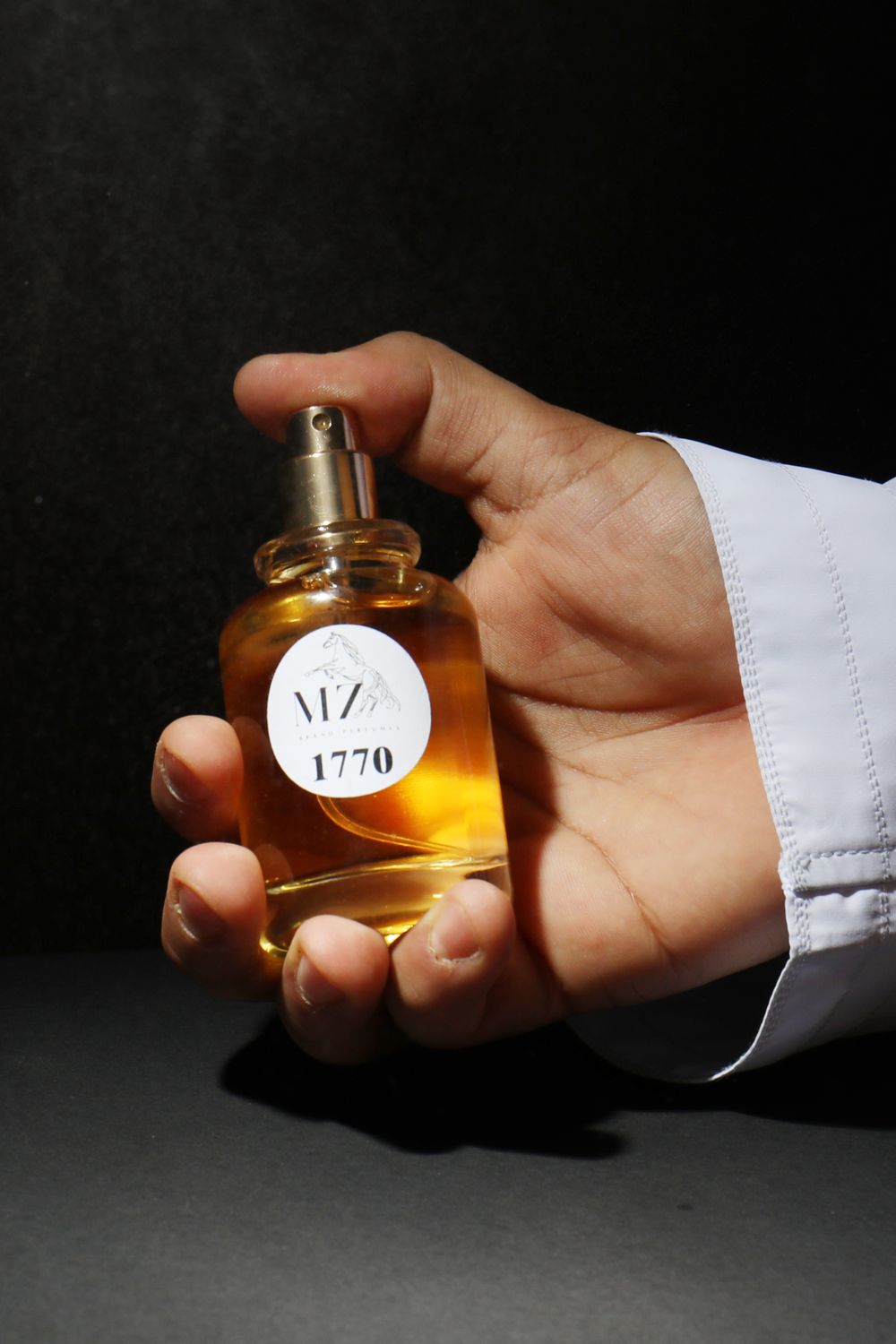 8 Men’s Fashion Choices That Scream “Notice Me Now.” 2 Close-up of a hand holding a perfume bottle with shadowed backdrop, emphasizing elegance.