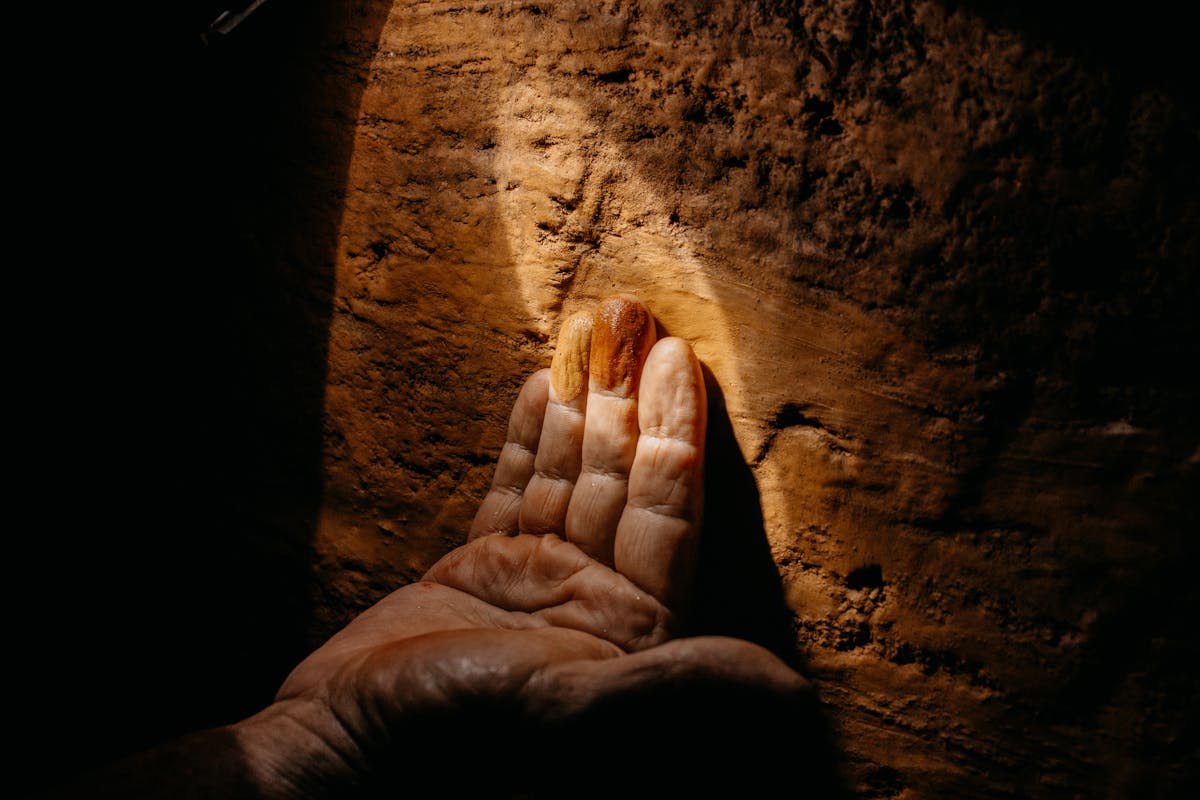 Close-up of a hand reaching towards a gemstone embedded in a mine wall, Ouro Preto, Brazil.