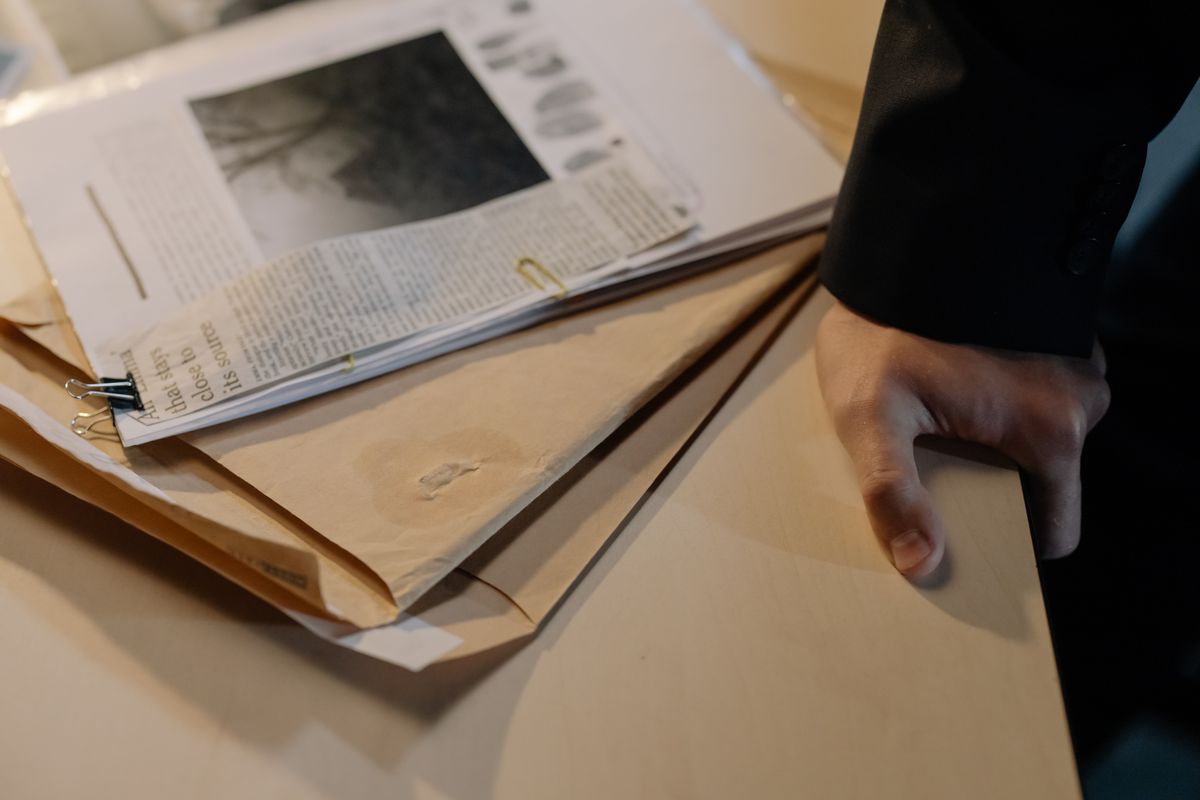 Statue of Liberty Boat Tragedy Leaves 2 Dead as Captain Faces 13 Charges 2 Close-up of a hand resting on a desk near a stack of investigative documents and newspaper clippings.