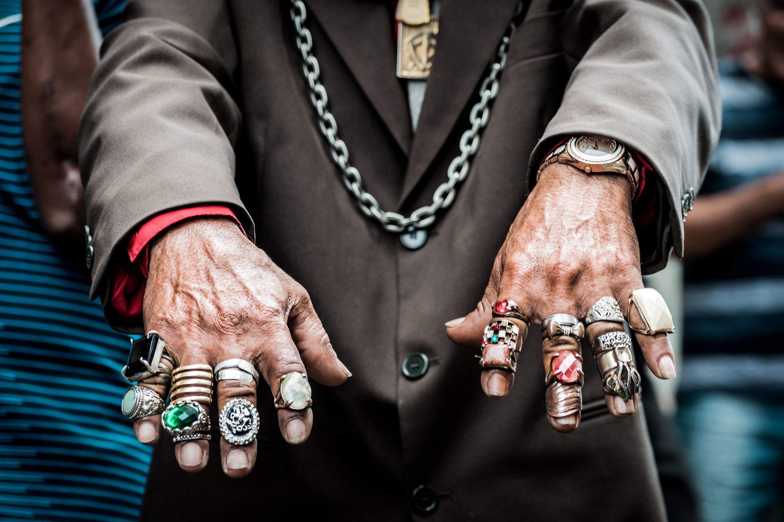 Close-up of a person's hands wearing multiple rings, a brown blazer, and a necklace.